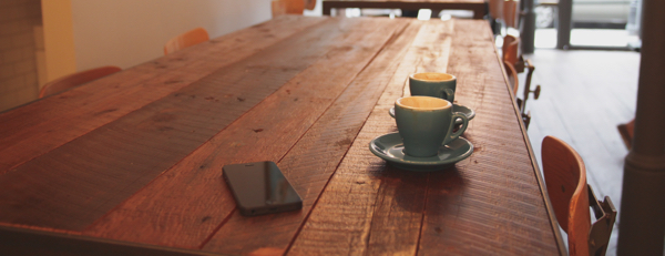 wooden table in a cafe with a deserted iphone and two coffee cups